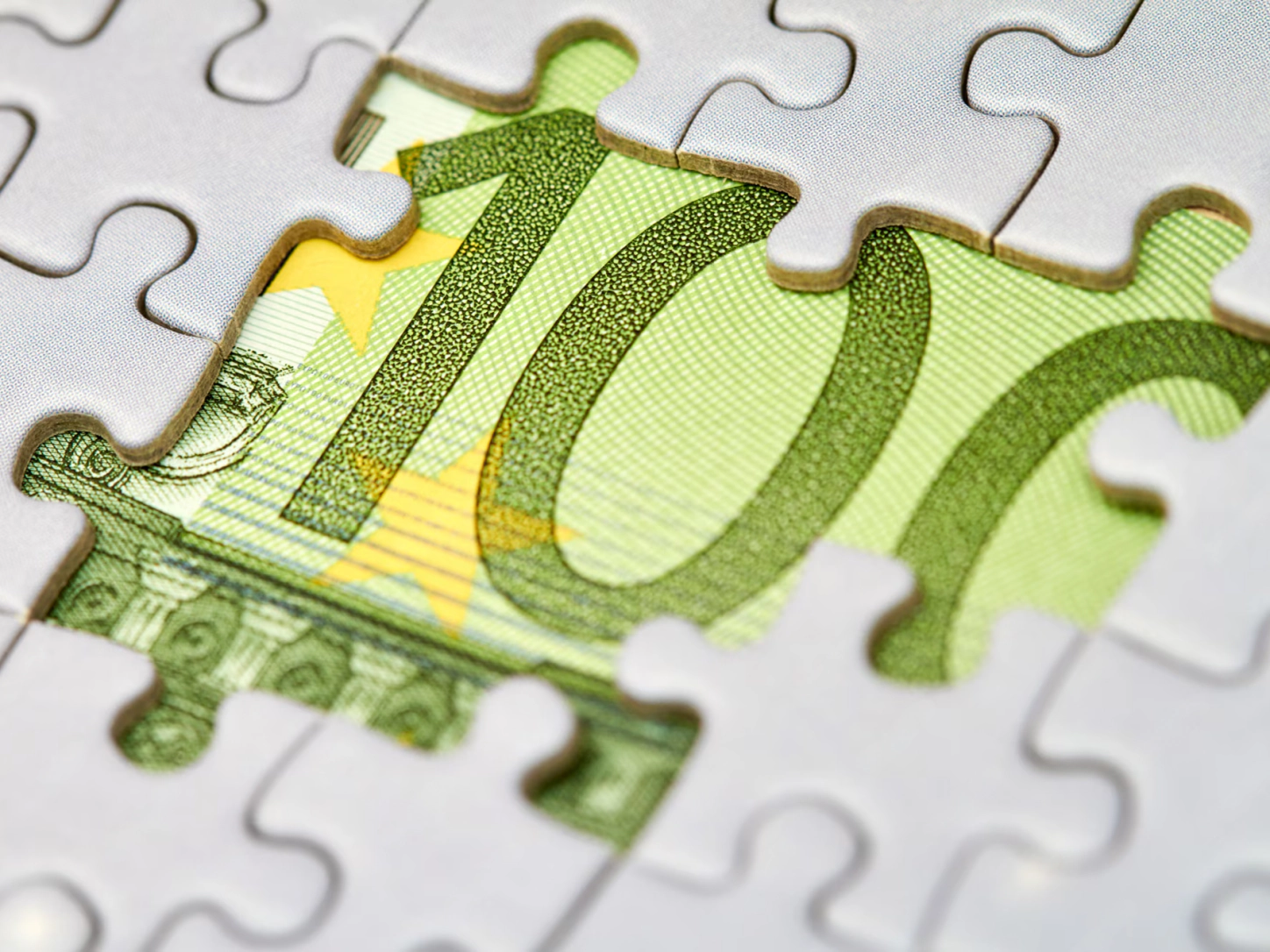 Un puzzle bianco con alcune tessere mancanti che lasciano vedere una banconota da 100 euro