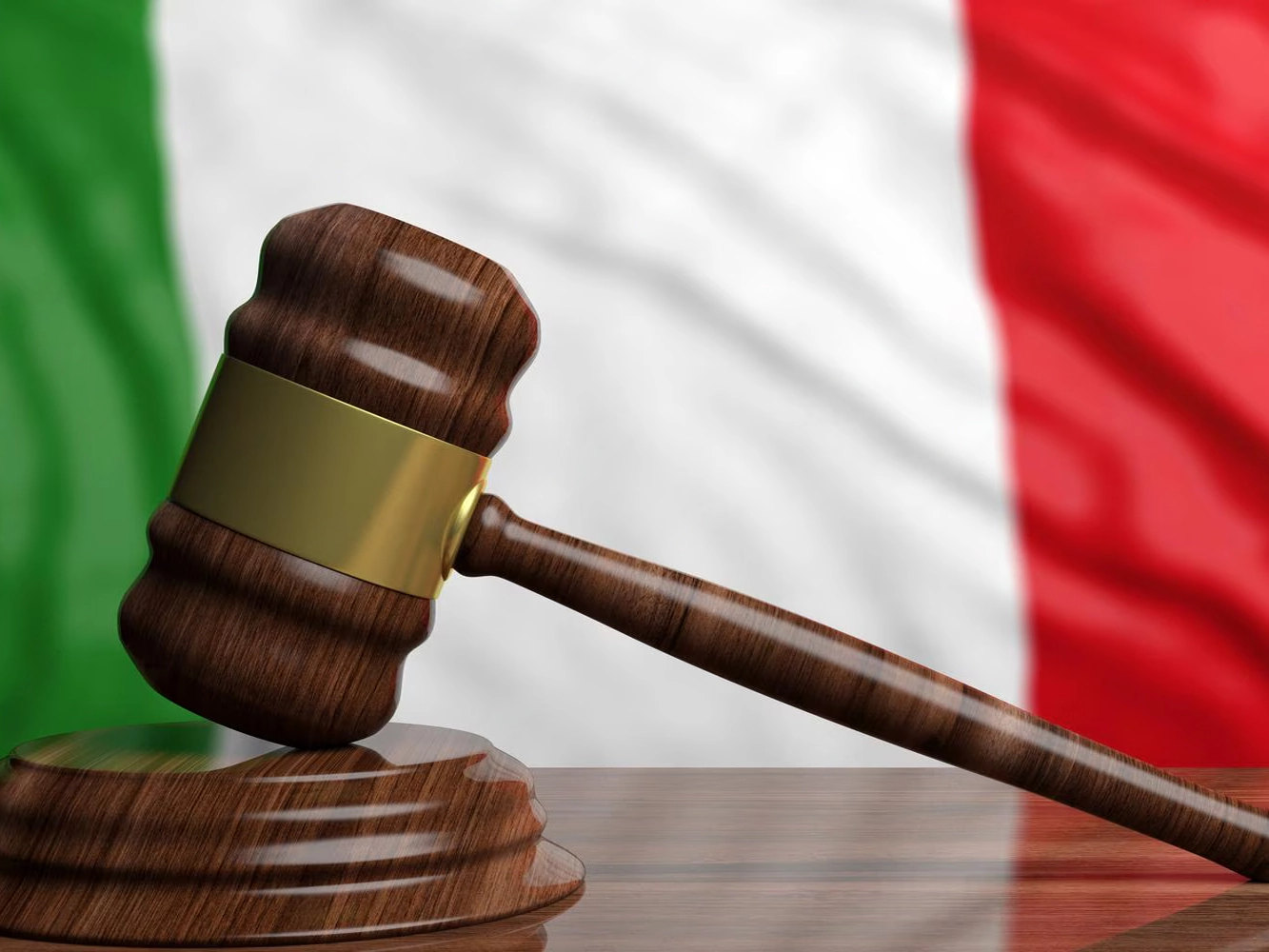 Un martelletto da giudice su un tavolo di legno, sullo sfondo la bandiera italiana